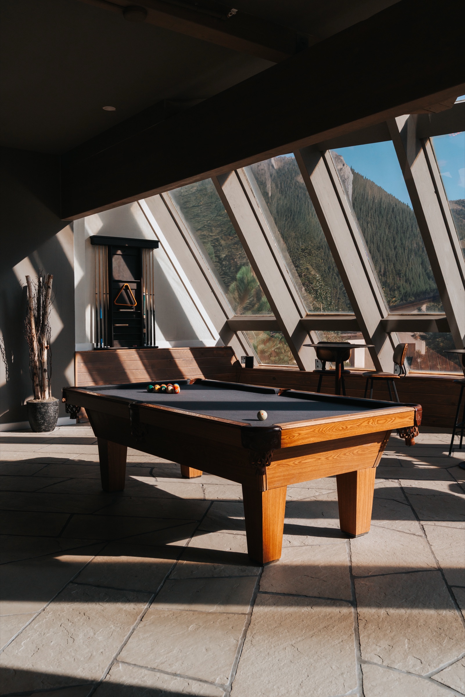 Pool table beneath the angled glass curtain wall, mountain ridge through windows