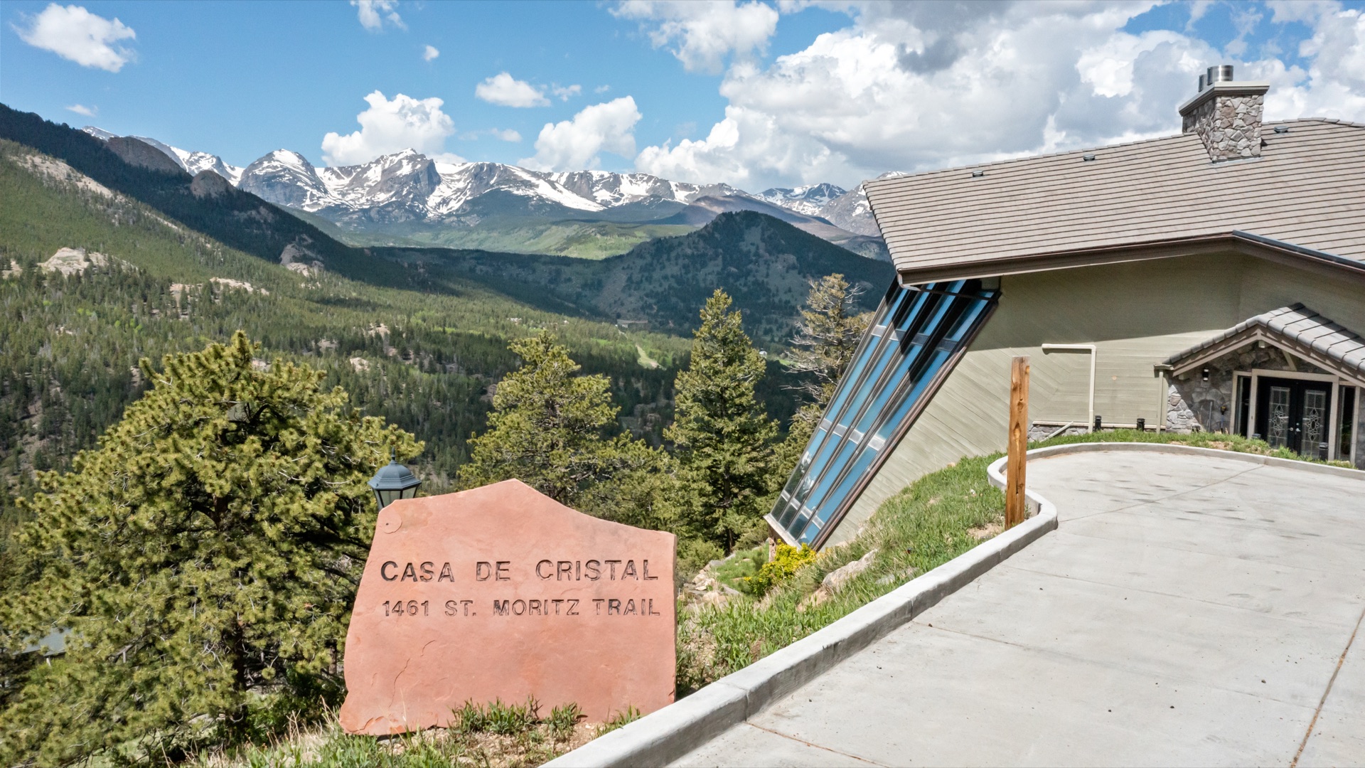 Casa de Cristal entrance with stone sign and Rocky Mountains in summer